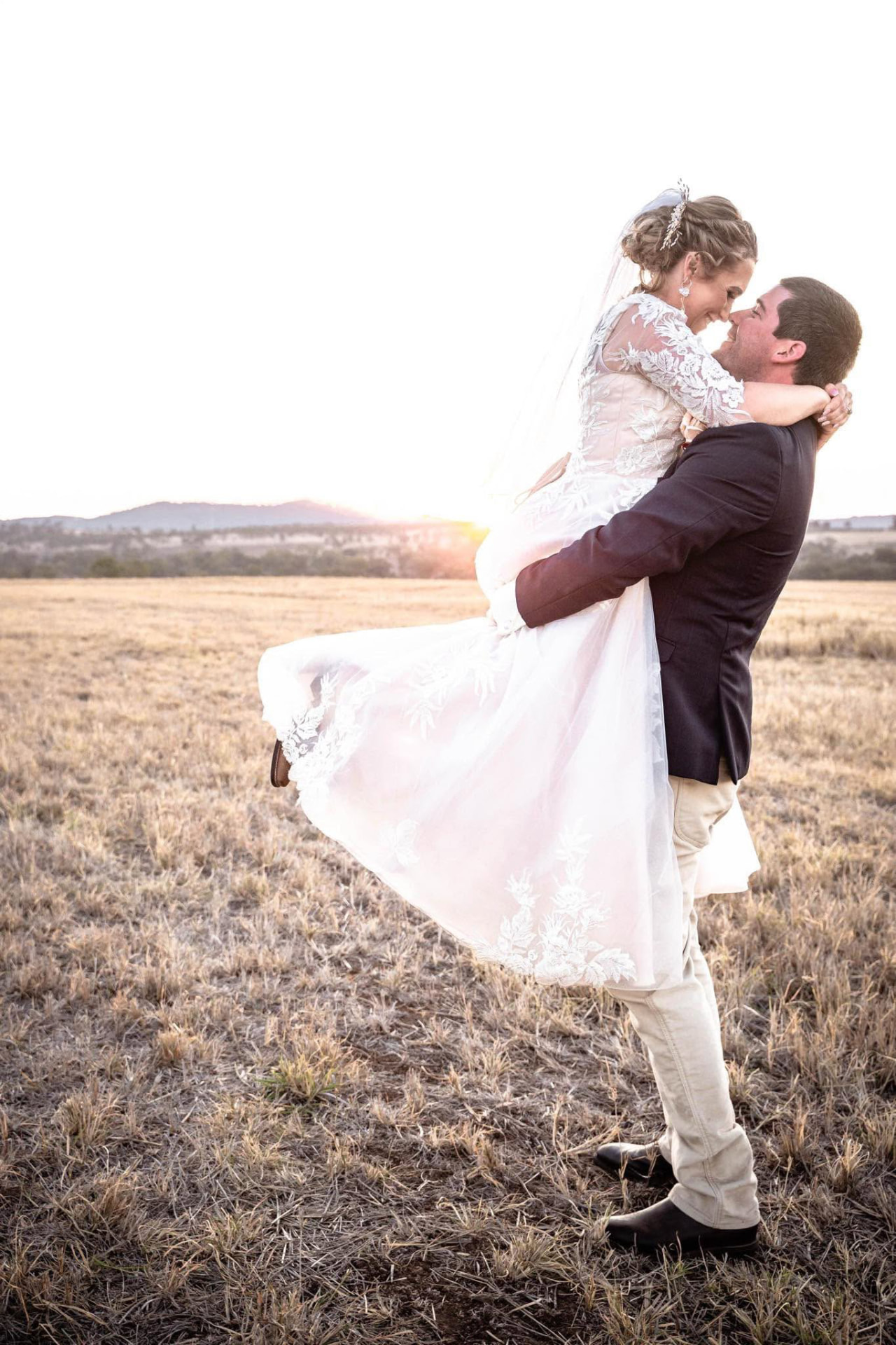 Groom lifting his bride at sunset in a golden country paddock