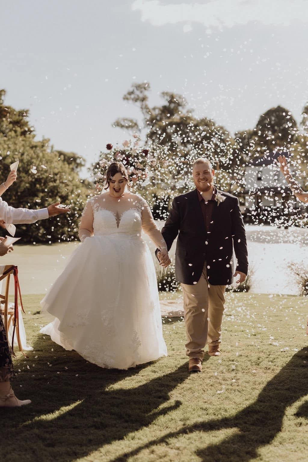 Newlyweds walking back down the aisle through a shower of confetti