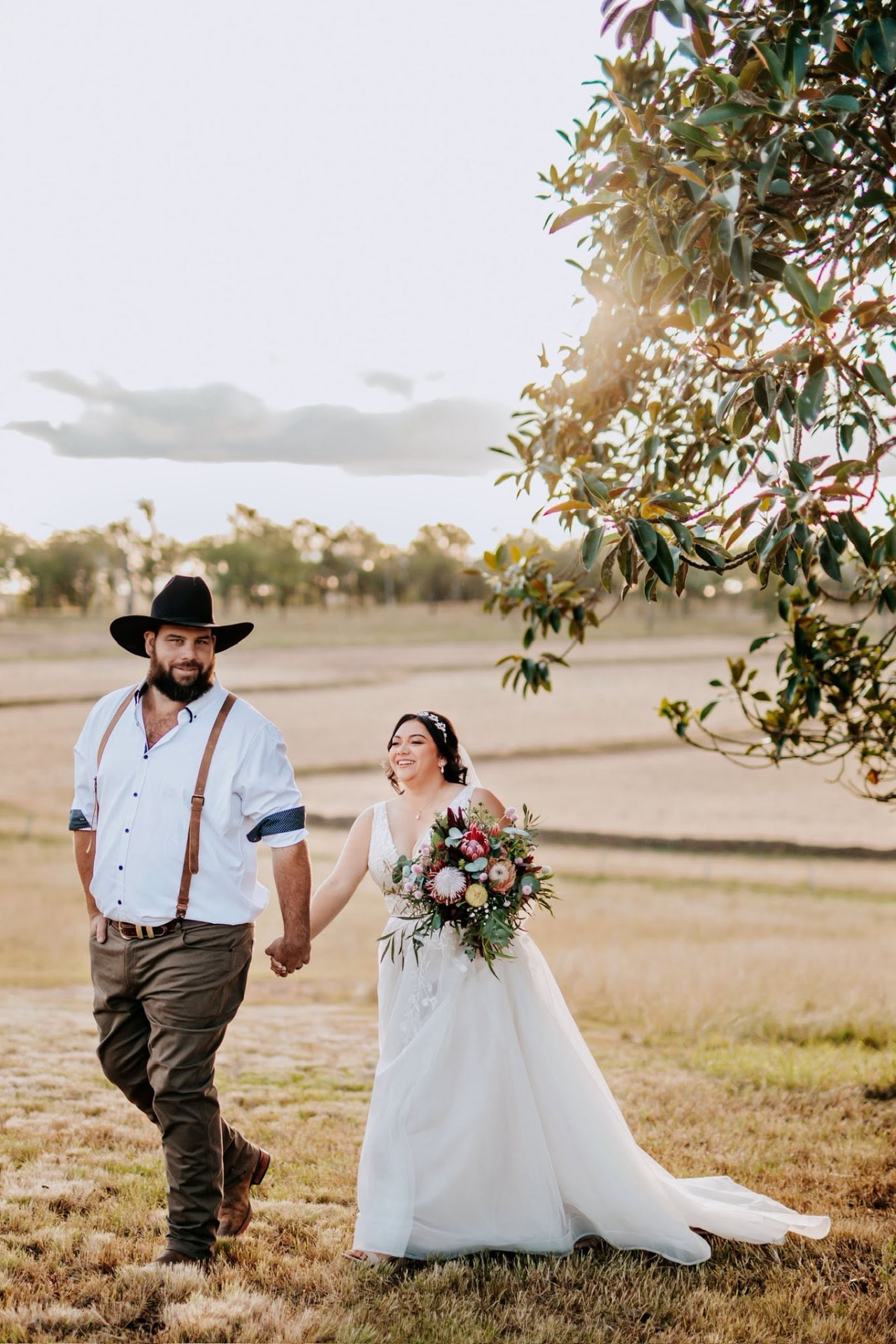 Newlyweds walking hand in hand through the paddock, bride carrying a native bouquet