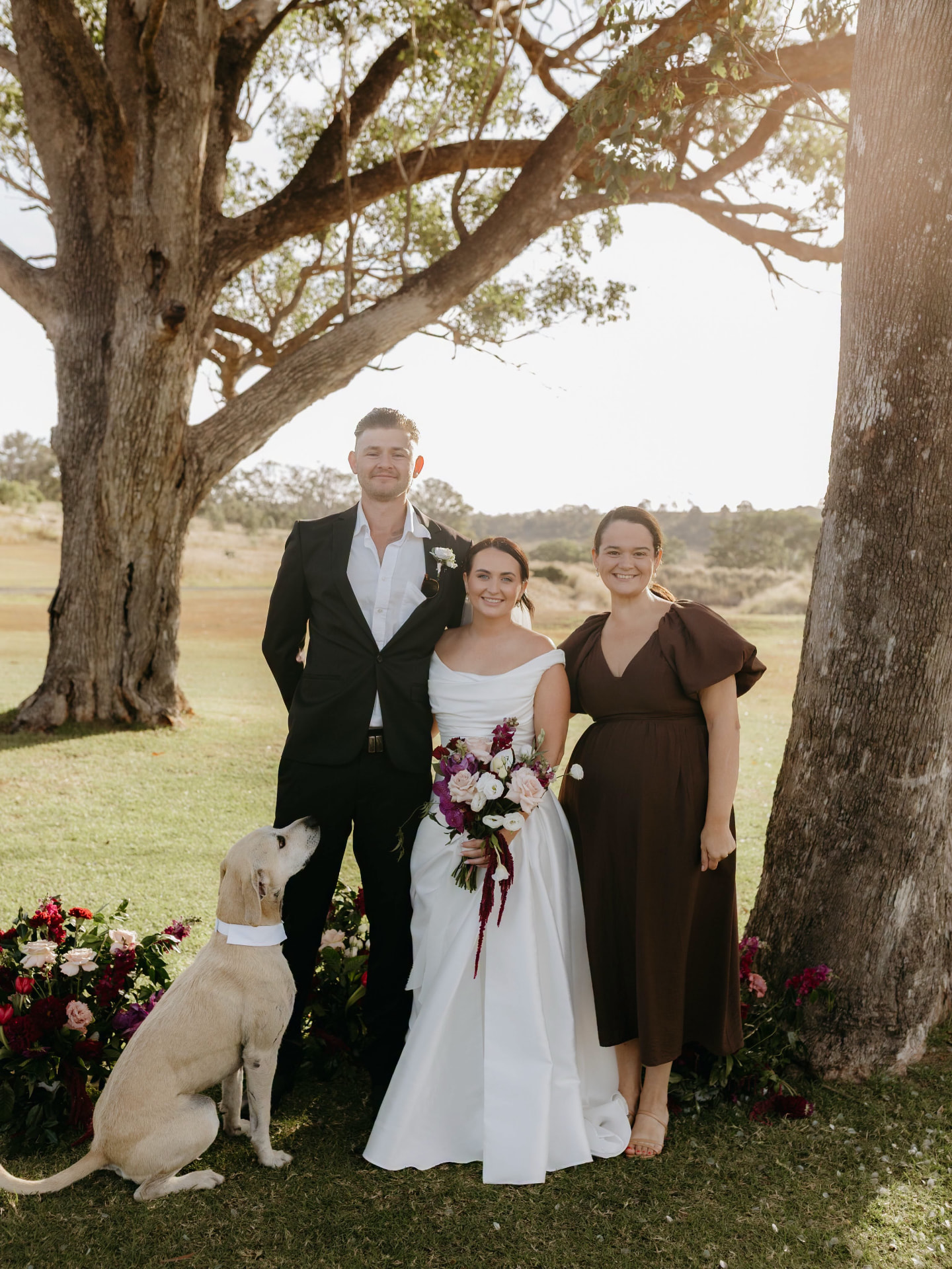 Simone with a couple and their dog beneath a gum tree at golden hour